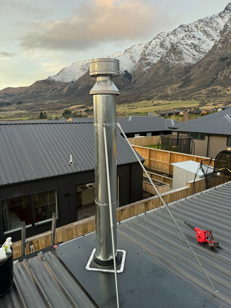 New stainless flue installed on a roof with the Remarkables mountain range behind
